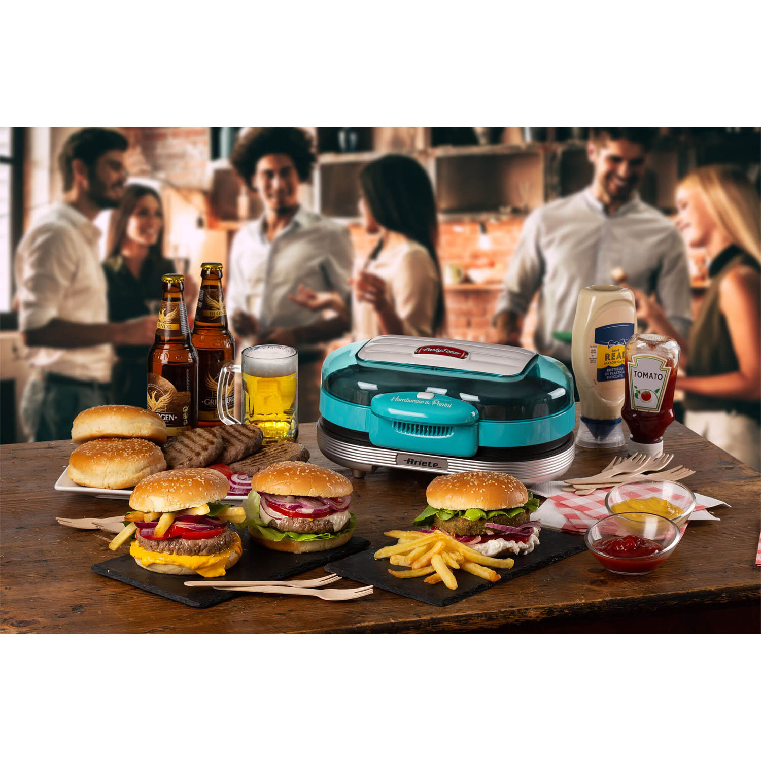 Tavolo con hamburger, patatine, birre, salse e un'hamburgeriera turchese, persone sullo sfondo.