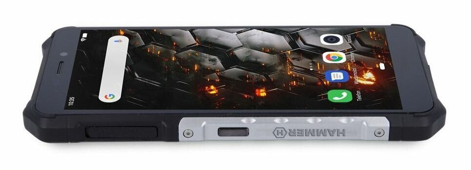 Wytrzymały smartfon w czarno-srebrnym designie. Ekran wyświetla aplikacje i czas. Tło przedstawia geometryczny wzór.