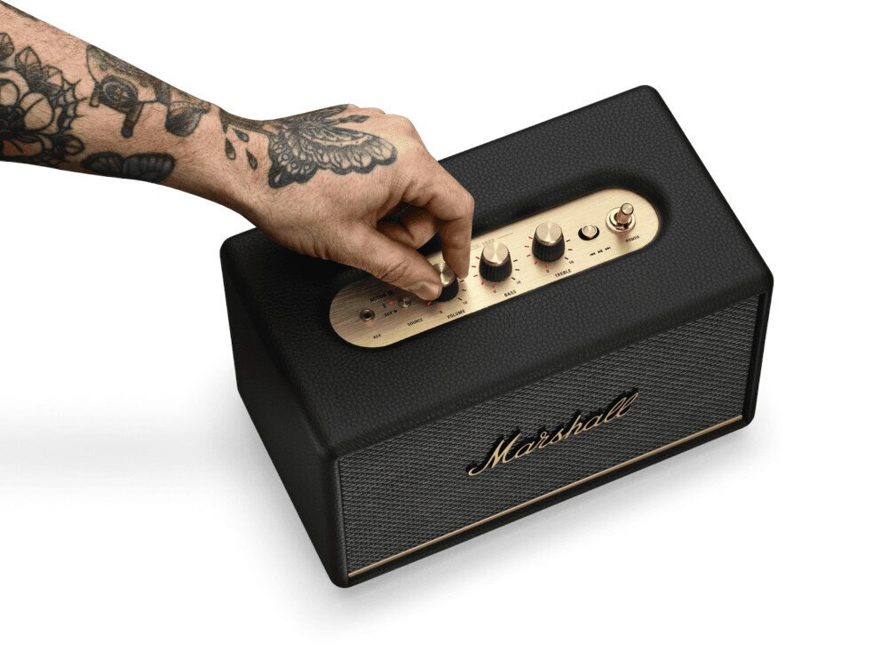 Dłoń regulująca pokrętło głośności na czarnym głośniku Marshall, zbliżenie.