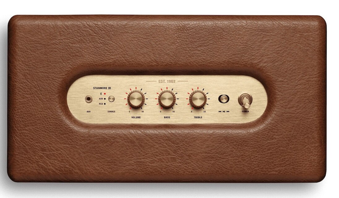 Brązowy skórzany głośnik ze złotym panelem sterowania, przyciskami i pokrętłami. Czarne tło.