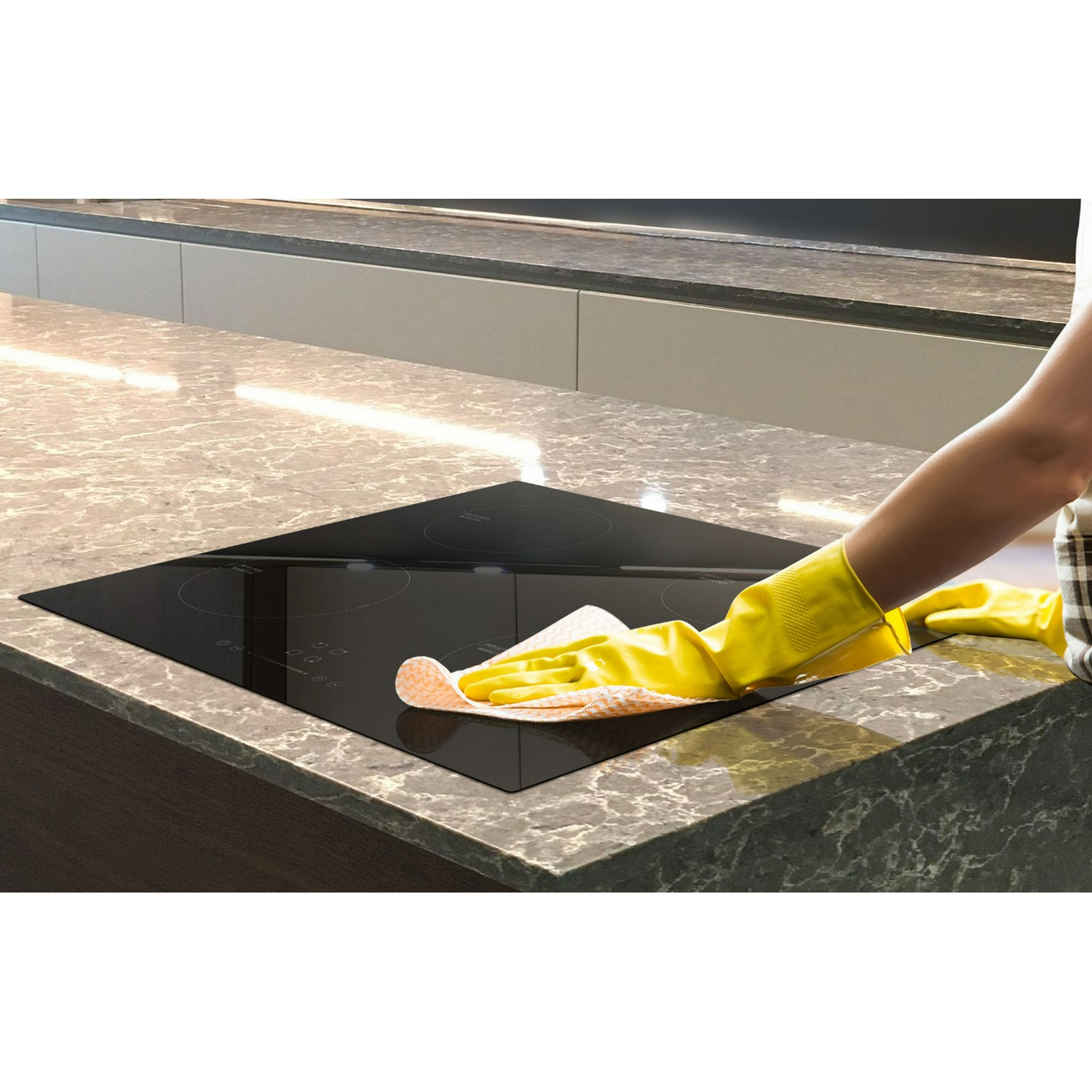 A person wearing yellow gloves cleans a black stovetop in a kitchen.