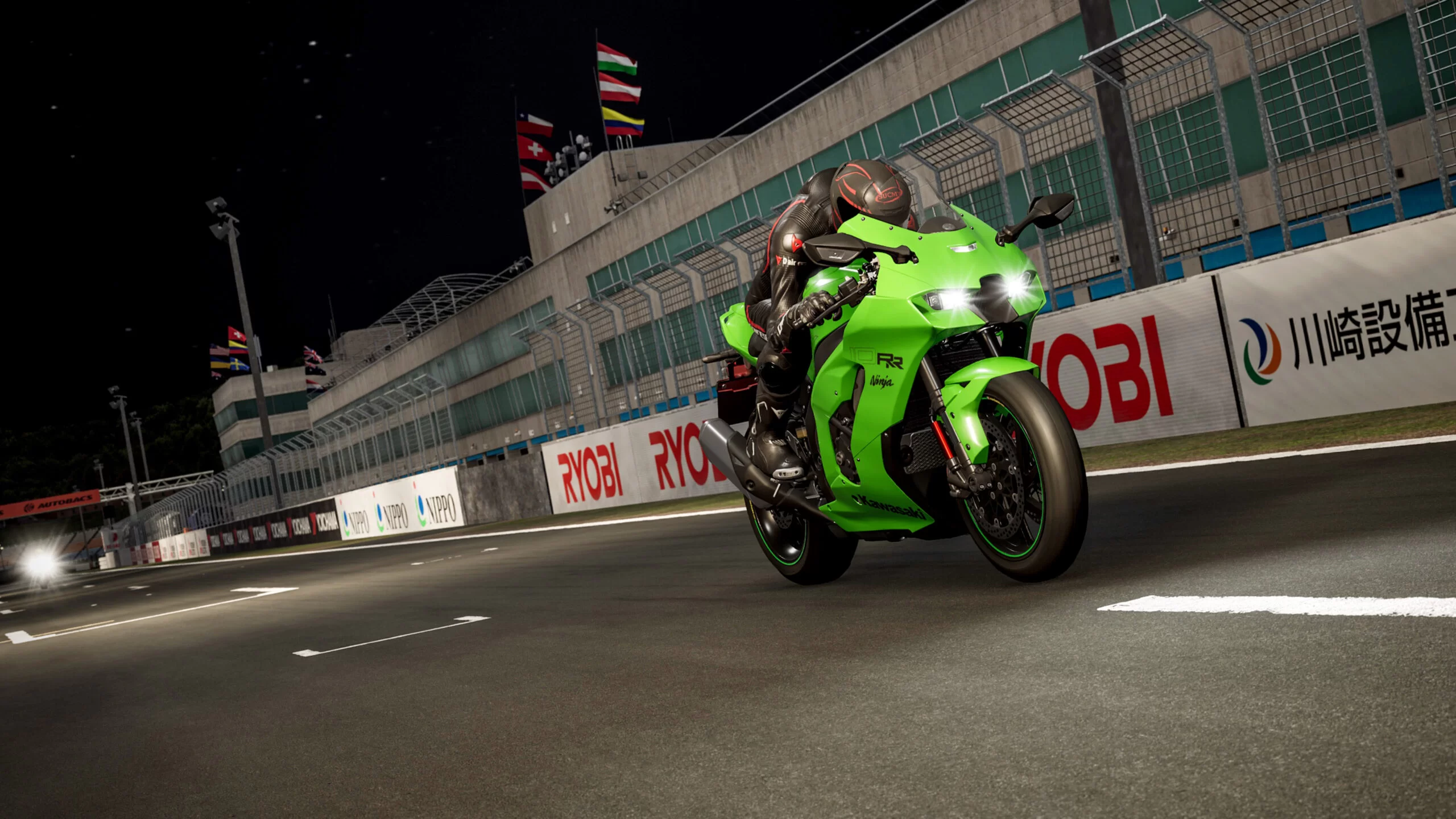 Una moto Kawasaki Ninja verde corre su una pista di notte, con luci e bandiere sullo sfondo.