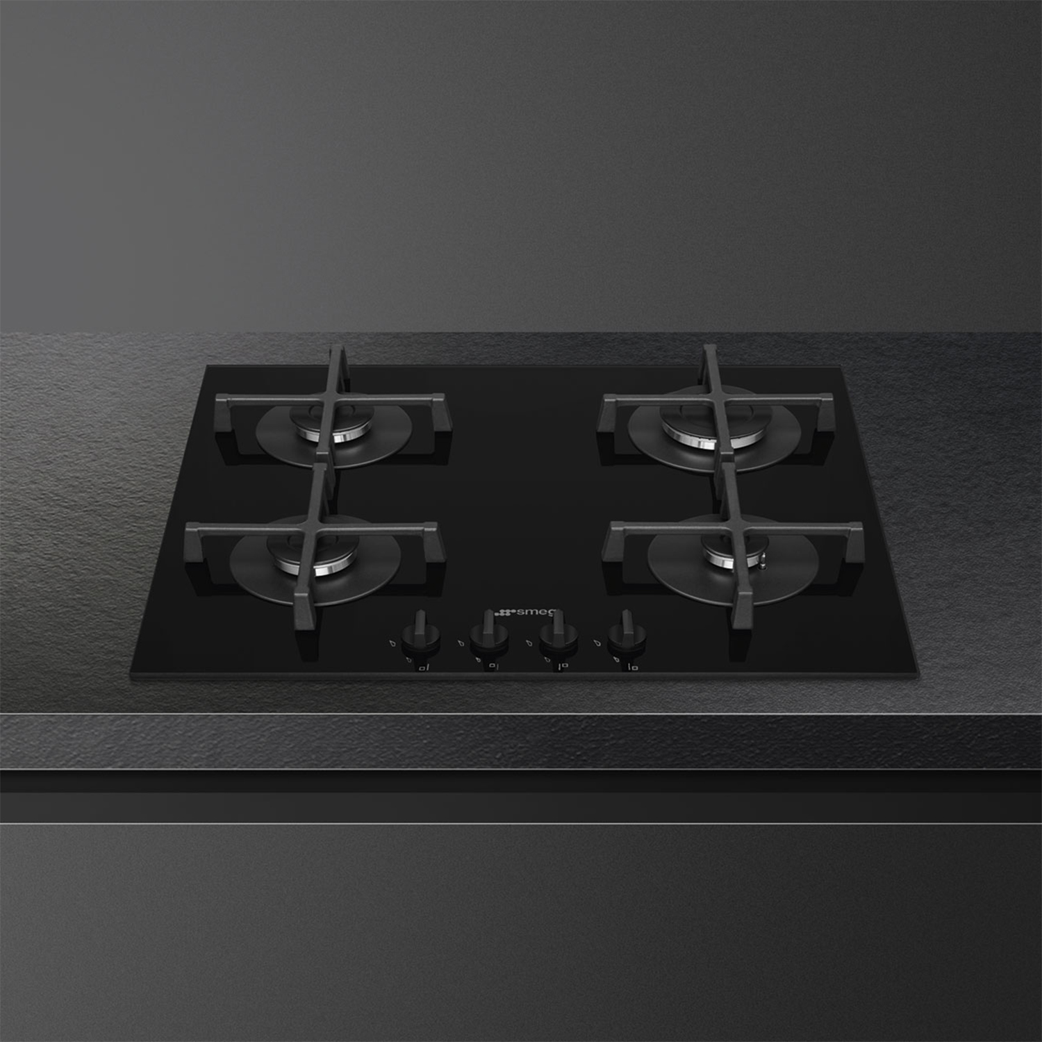 Un piano cottura a induzione Smeg nero con quattro fuochi su una superficie grigio scuro.