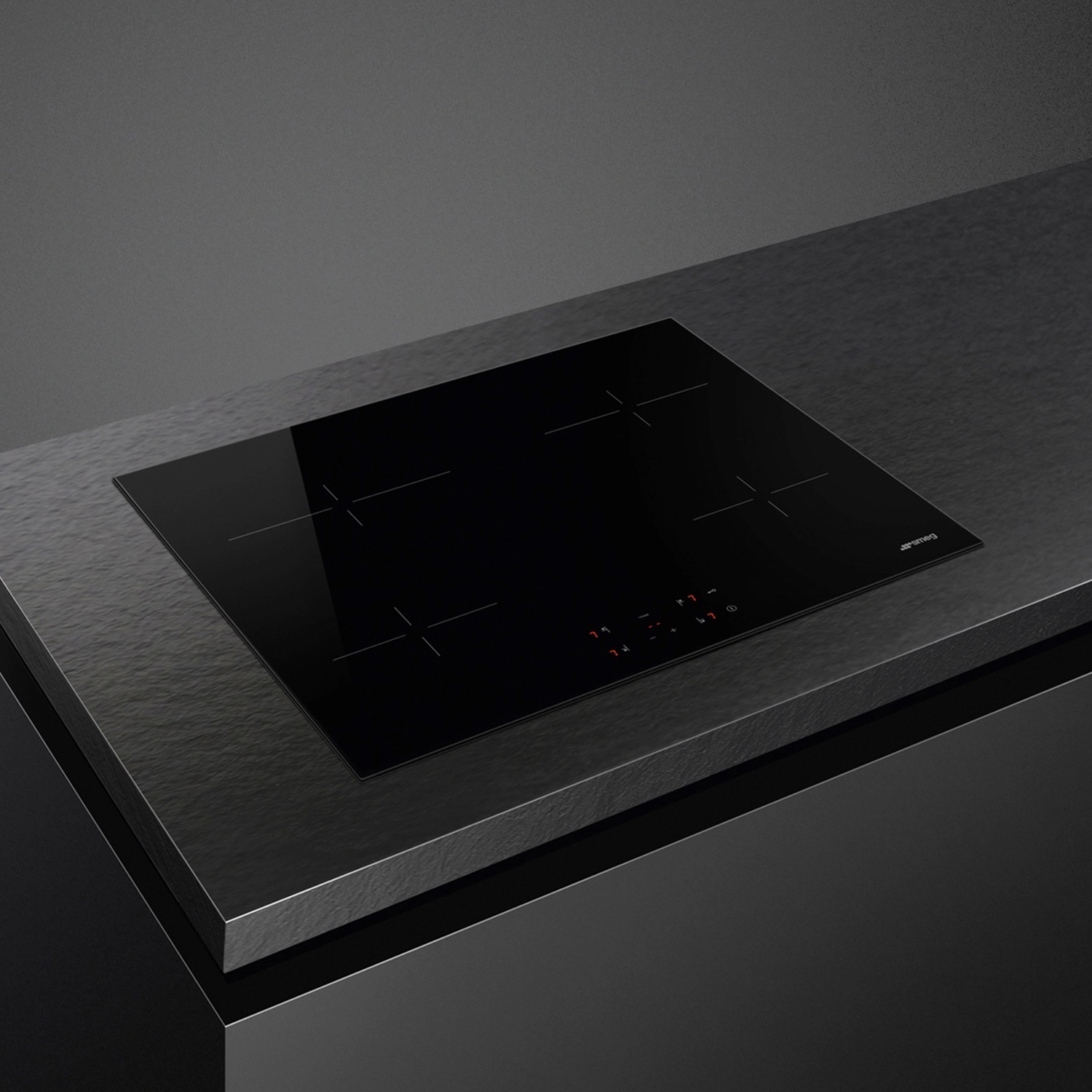 Piano cottura a induzione nero su superficie scura con comandi touch e logo Smeg.