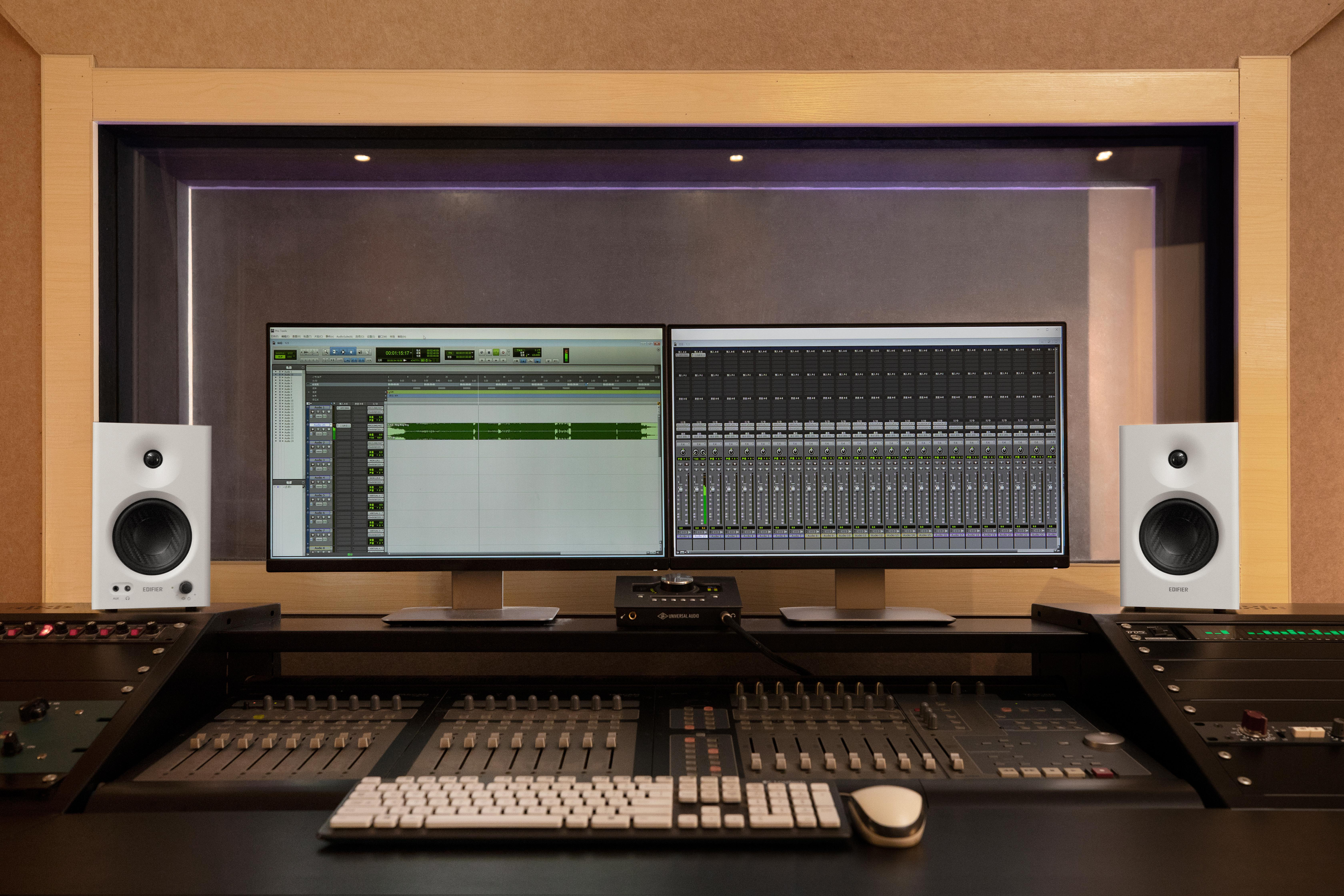 Tonstudio-Setup: Zwei Monitore, Mischpult, Lautsprecher und Tontechnik.
