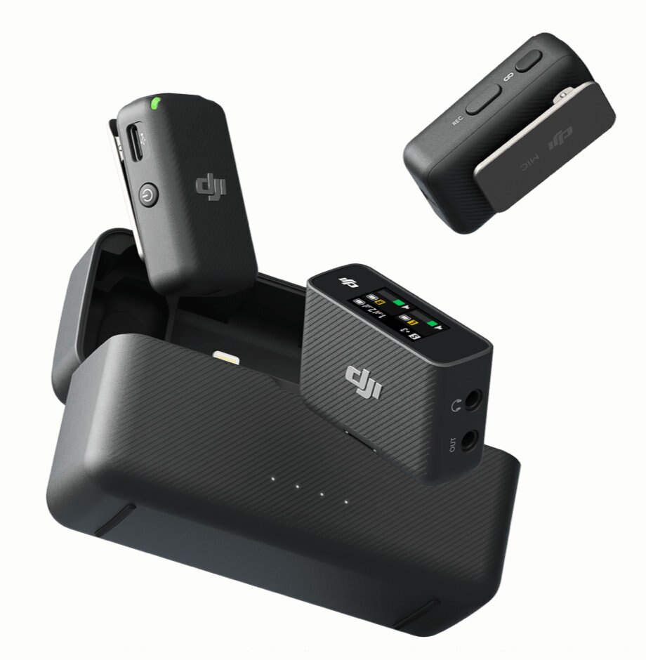 Czarny sprzęt audio z etui ładującym. Zawiera mikrofon i mały wyświetlacz.