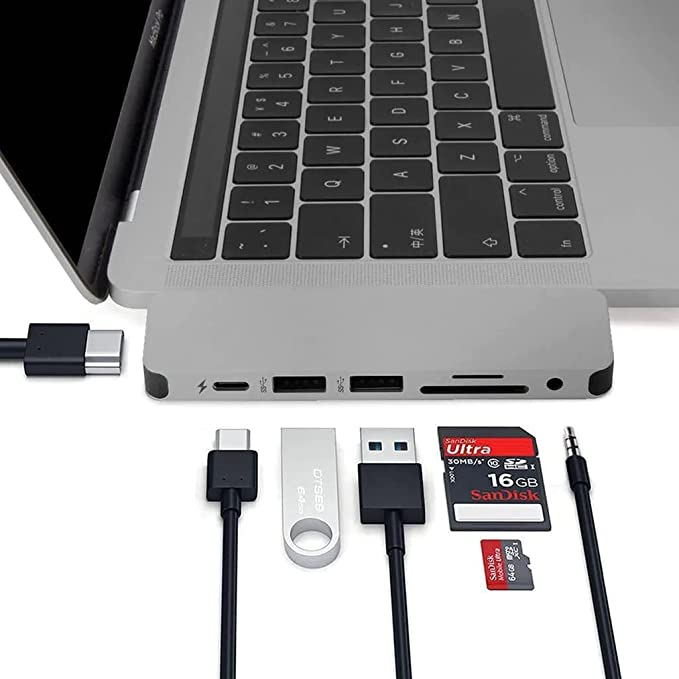 Un portátil con un concentrador USB conectado y varios accesorios: cable USB-C, unidad flash, tarjeta SD y conector de audio.