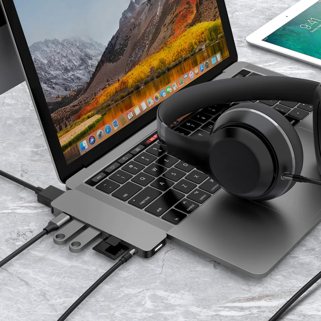 Laptop con concentrador, auriculares y tableta sobre una superficie texturizada. Cables conectados.