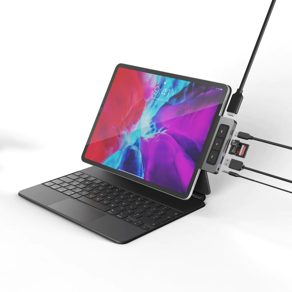 Un iPad con teclado conectado a un concentrador USB con accesorios: cable USB-C, tarjeta SD, conector de audio y botones.