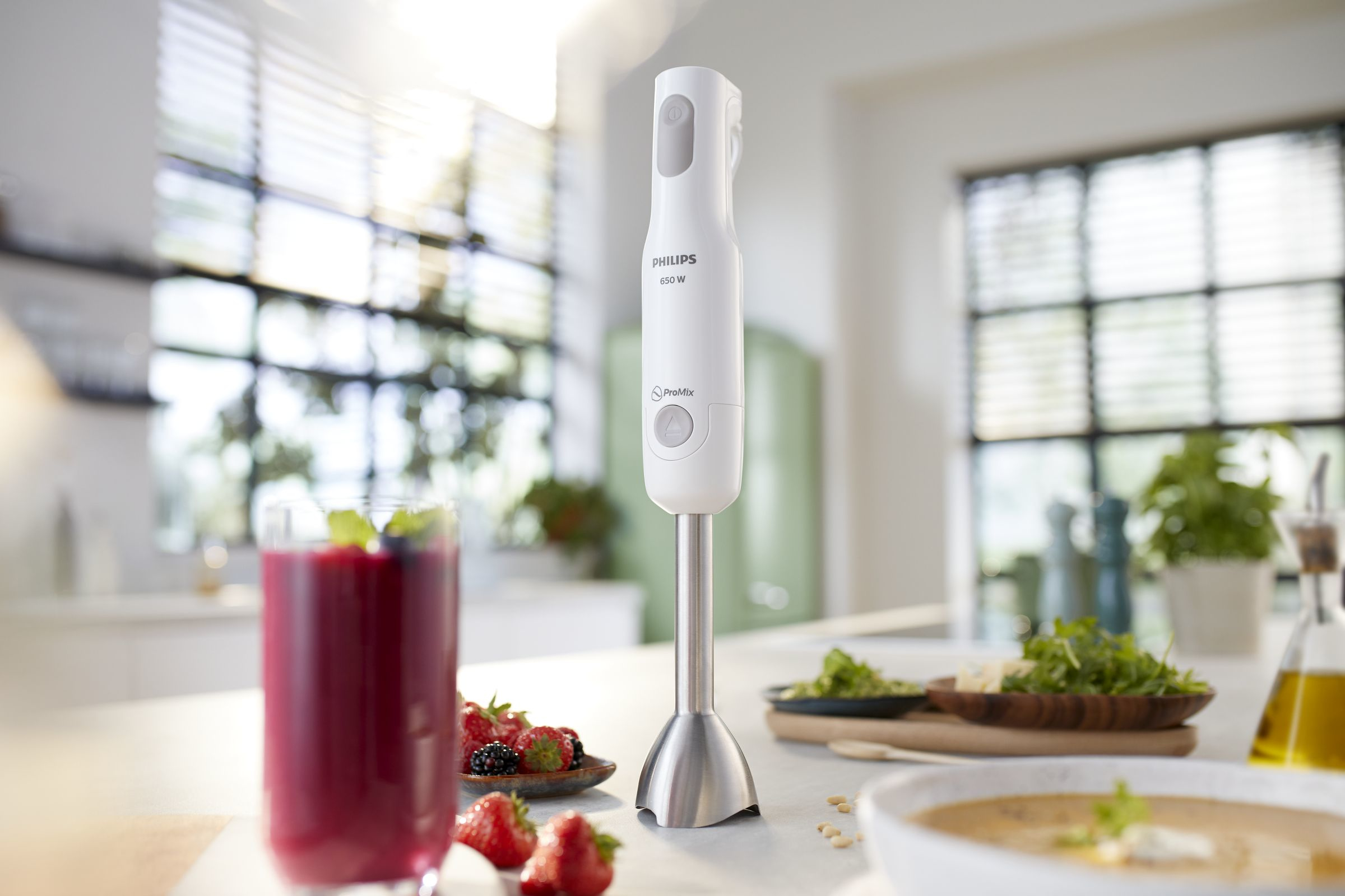 White hand blender with food items like berries, soup, and a glass of smoothie.