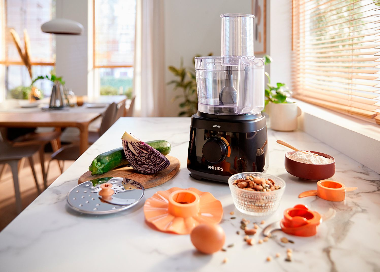 Food processor with ingredients on a marble countertop. Vegetables, nuts, and flour are visible.