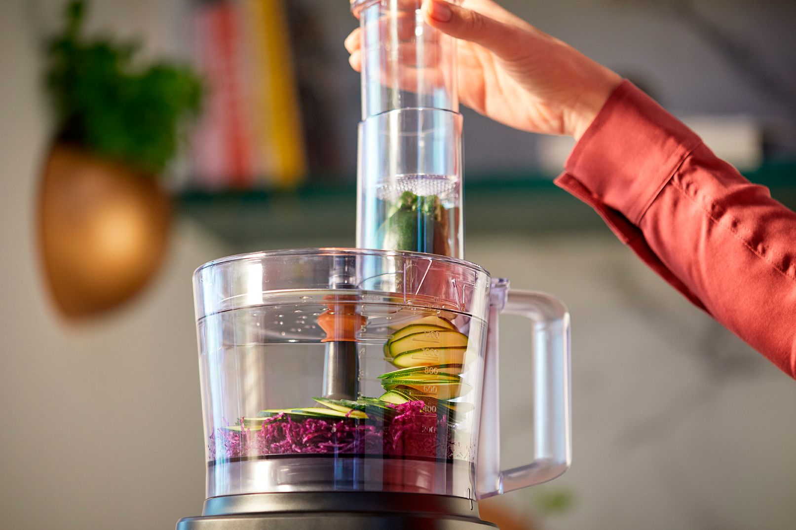 A food processor with vegetables inside and a hand holding the top lid.