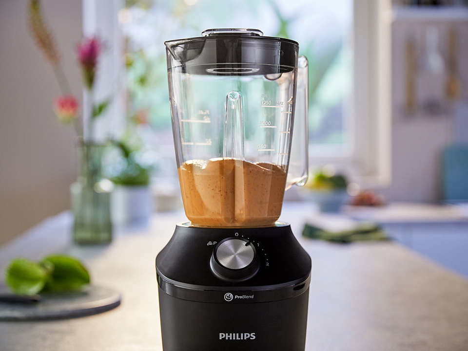 Black blender with a container full of orange-brown liquid, in a kitchen setting.