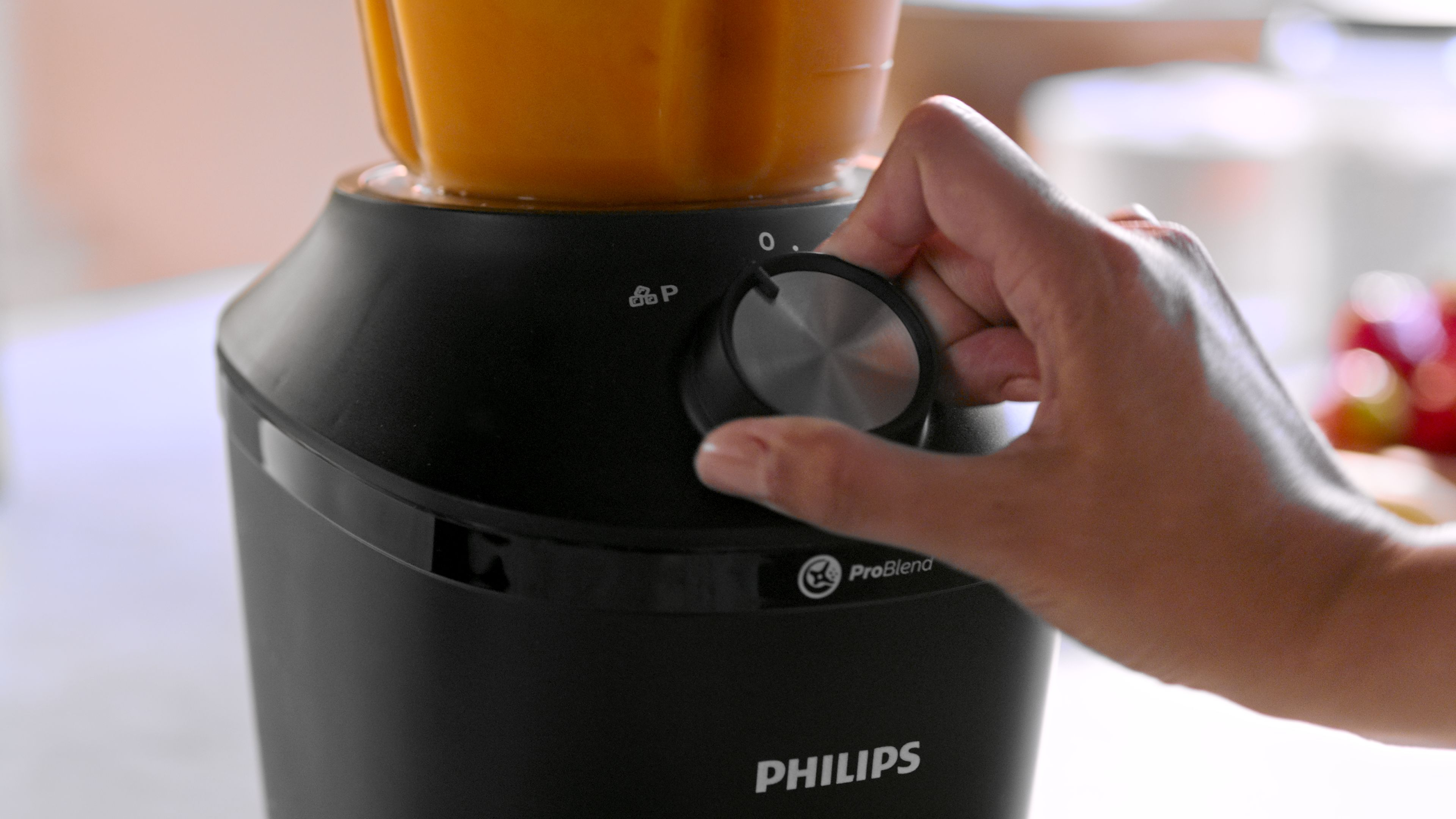 Hand turning a blender dial, filled with orange liquid, Philips ProBlend visible.