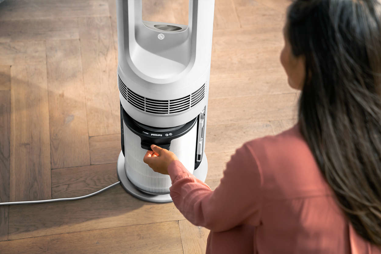 Woman adjusting the filter on a white Philips air purifier. The purifier is on a wooden floor.