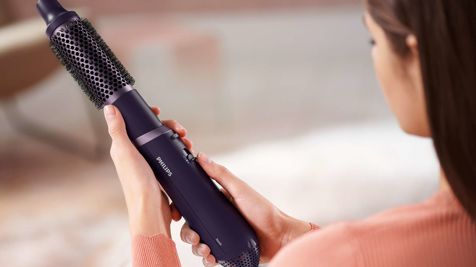 Een vrouw houdt een paarse en zwarte haarstyler vast, met de productnaam 'Philips'.
