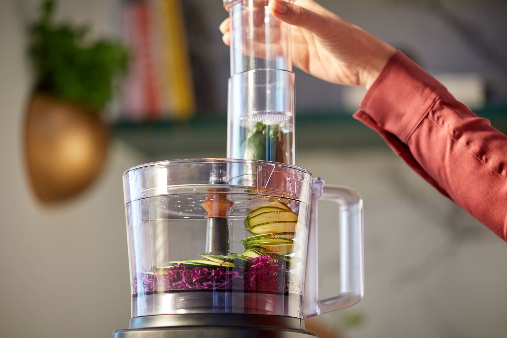 A person adding ingredients into a food processor. The processor is mostly transparent.