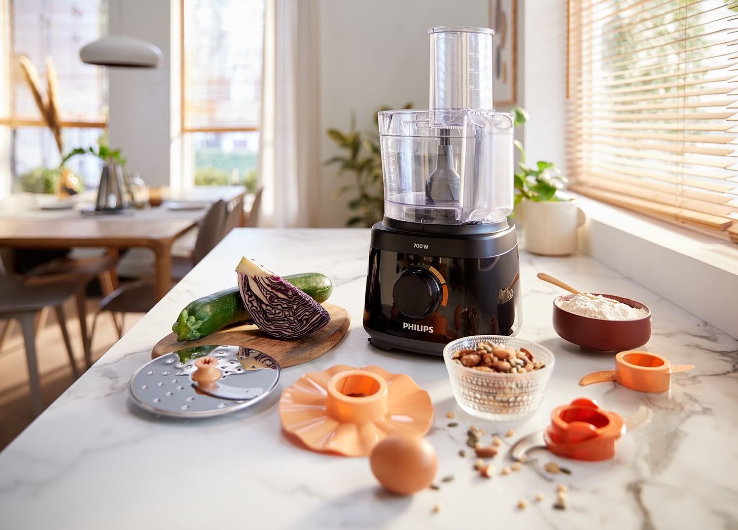 Food processor with ingredients like zucchini, red cabbage, and nuts, on a counter.