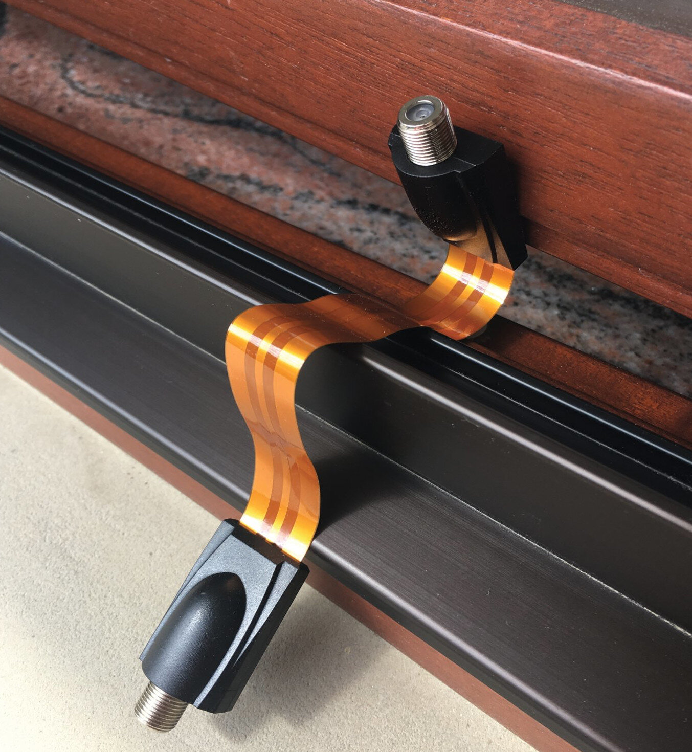 Zbliżenie kabla z elastycznym pomarańczowym odcinkiem, przymocowanym do ramy okiennej.