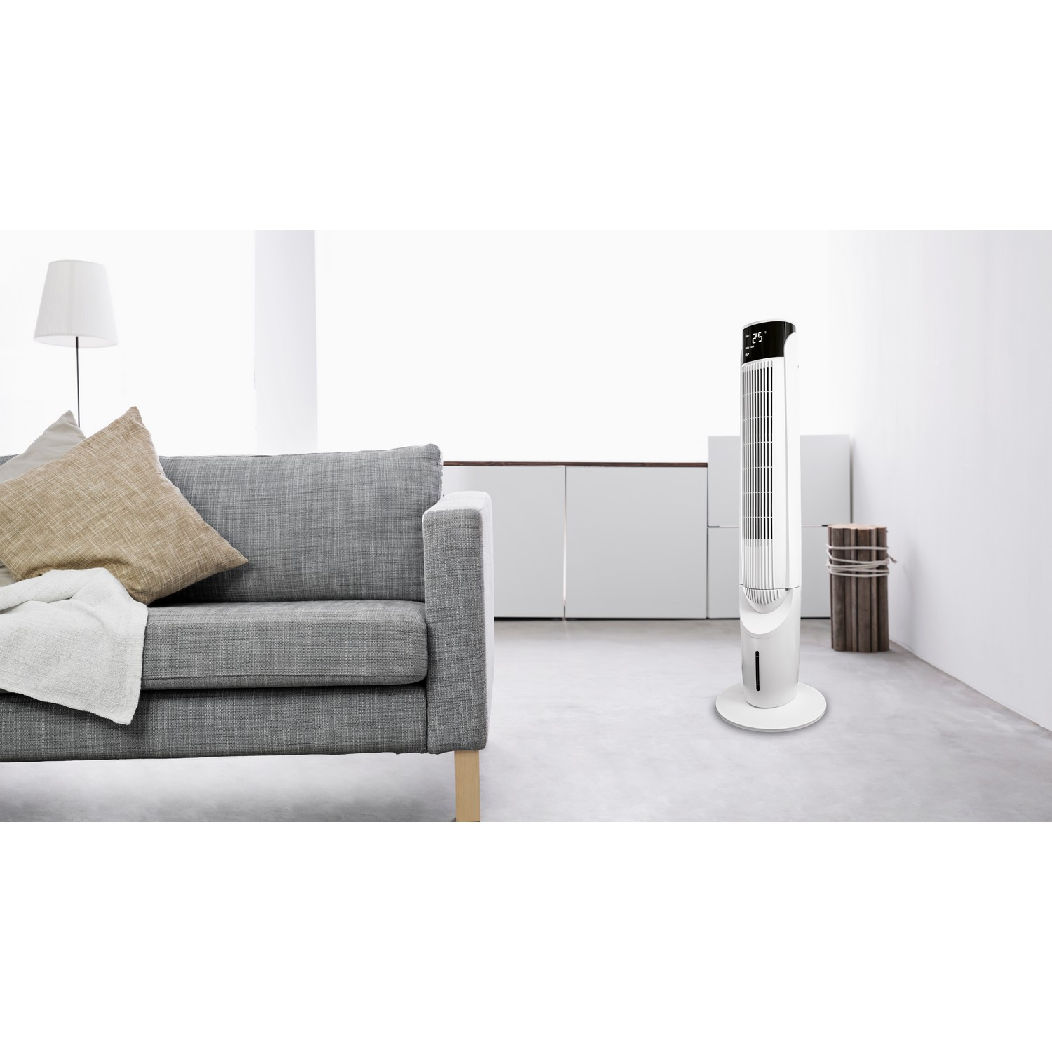 Un ventilateur tour blanc et fin se trouve à côté d'un canapé dans une pièce lumineuse.