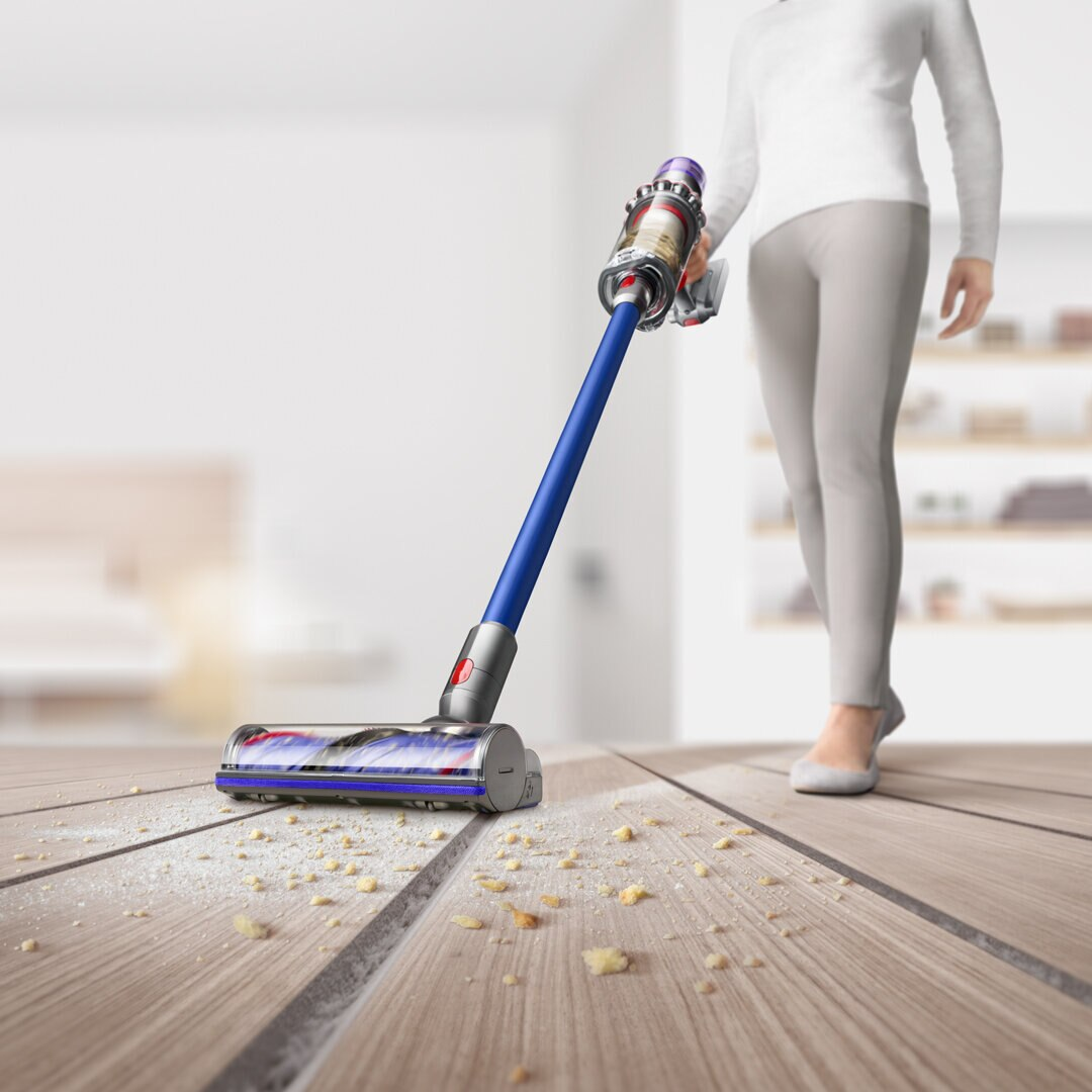 Kobieta odkurza drewnianą podłogę odkurzaczem pionowym Dyson.