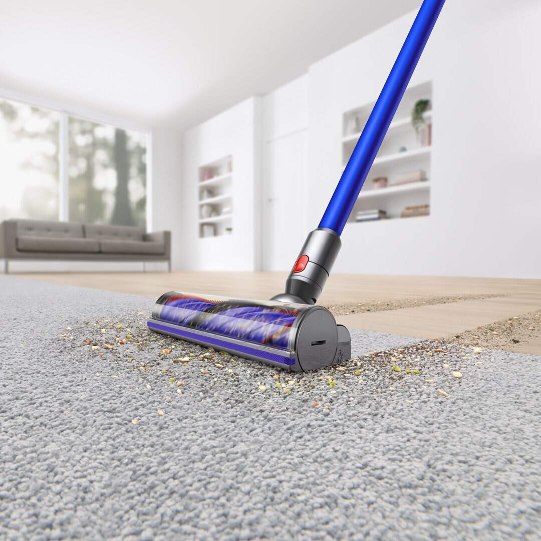 Niebiesko-srebrna głowica odkurzacza czyści szary dywan z resztek.