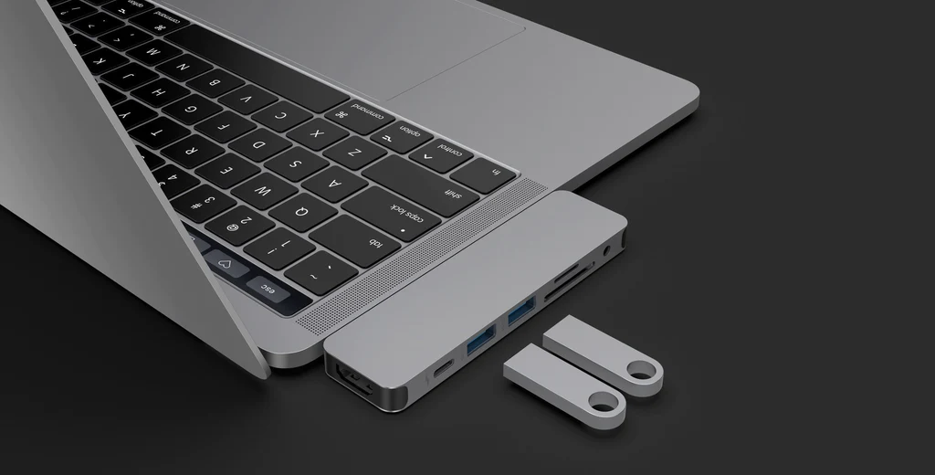 Portátil plateado con un concentrador USB y dos unidades USB. Fondo negro.