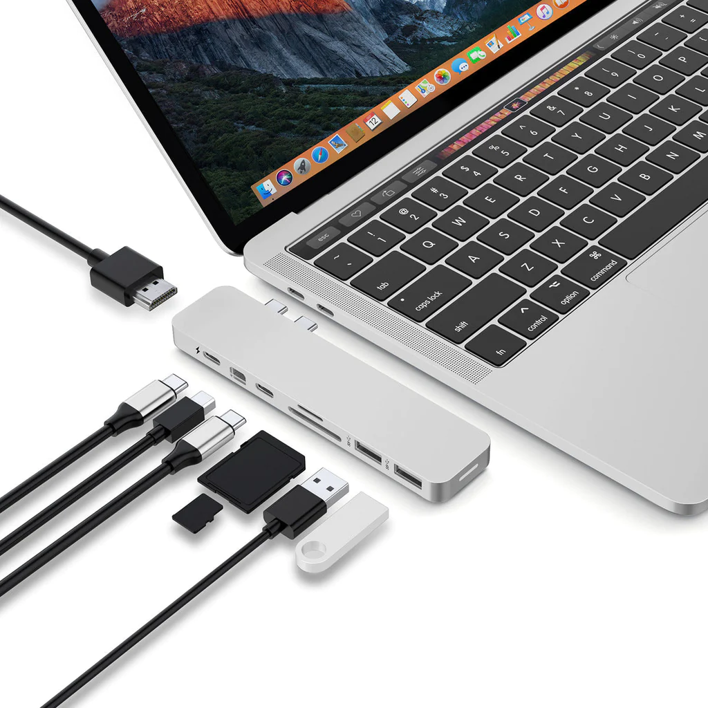 Un portátil conectado a múltiples cables y accesorios, incluyendo un hub USB, sobre una superficie blanca.