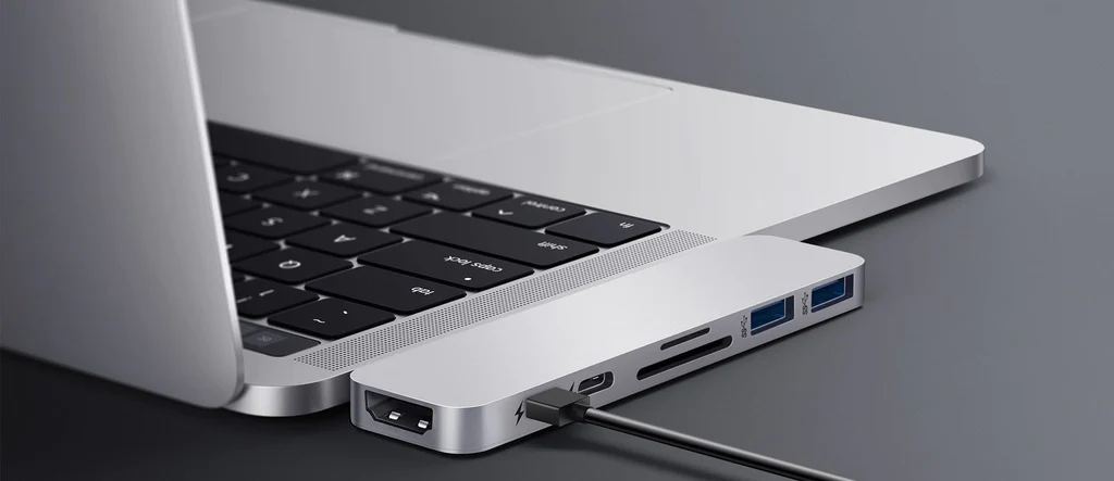 Un portátil conectado a un hub plateado con puertos.
