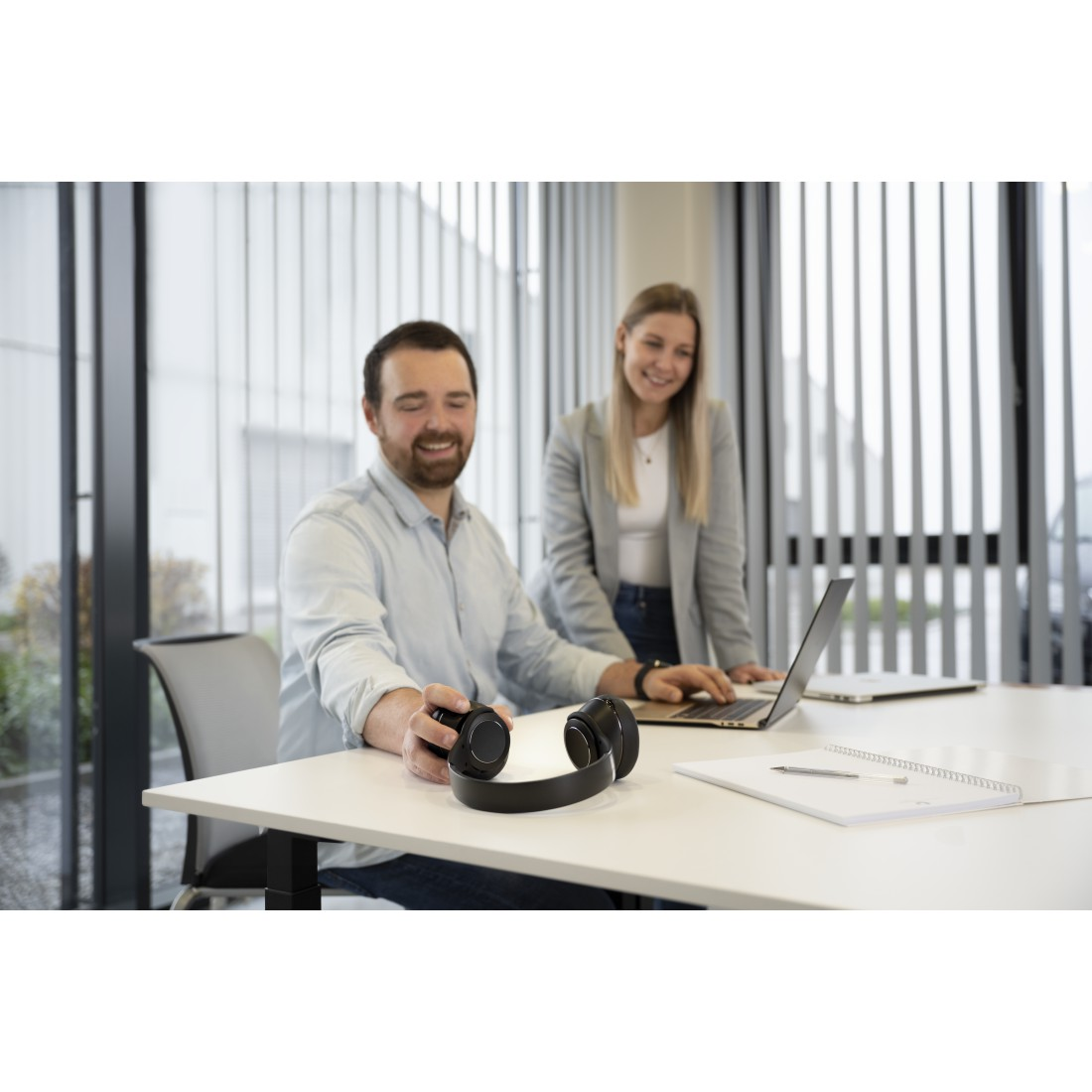 Mann und Frau im Büro, Mann hält Kopfhörer, Laptop auf dem Tisch.