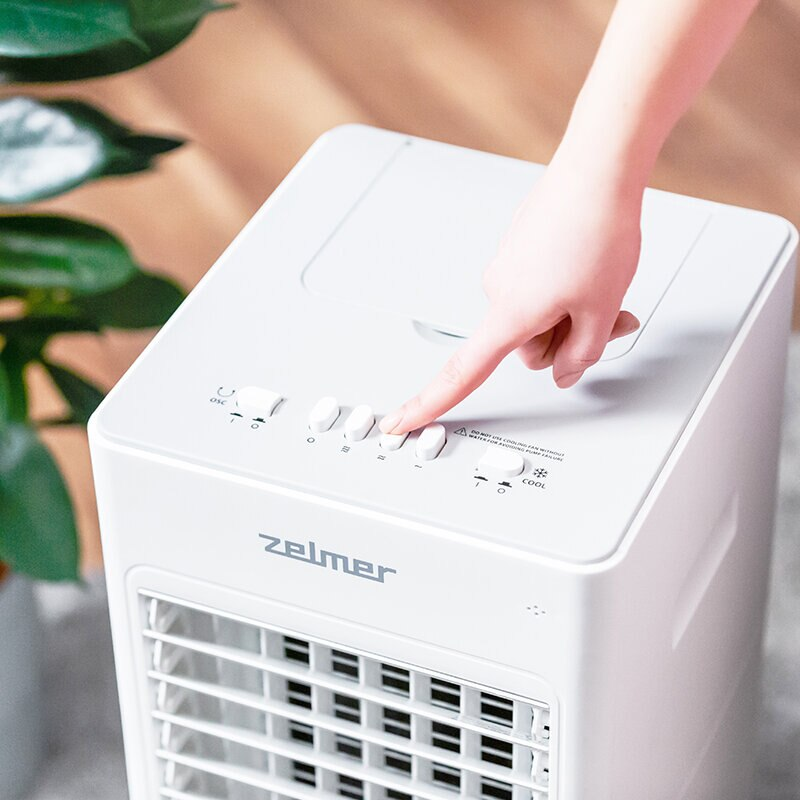 Ręka naciska przyciski na białym klimatyzatorze.