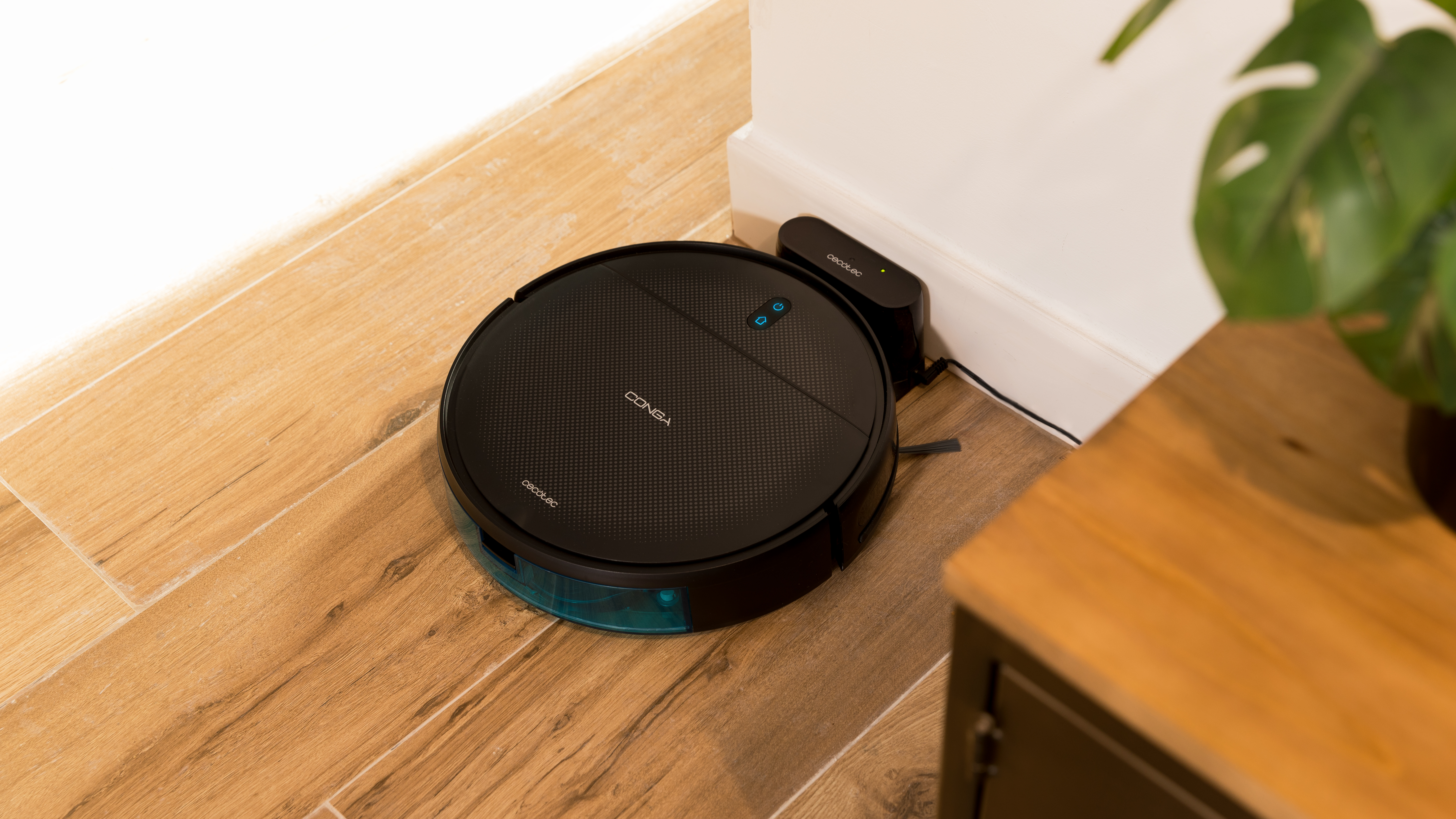 Una aspiradora robot negra en un piso de madera, con una estación de carga.