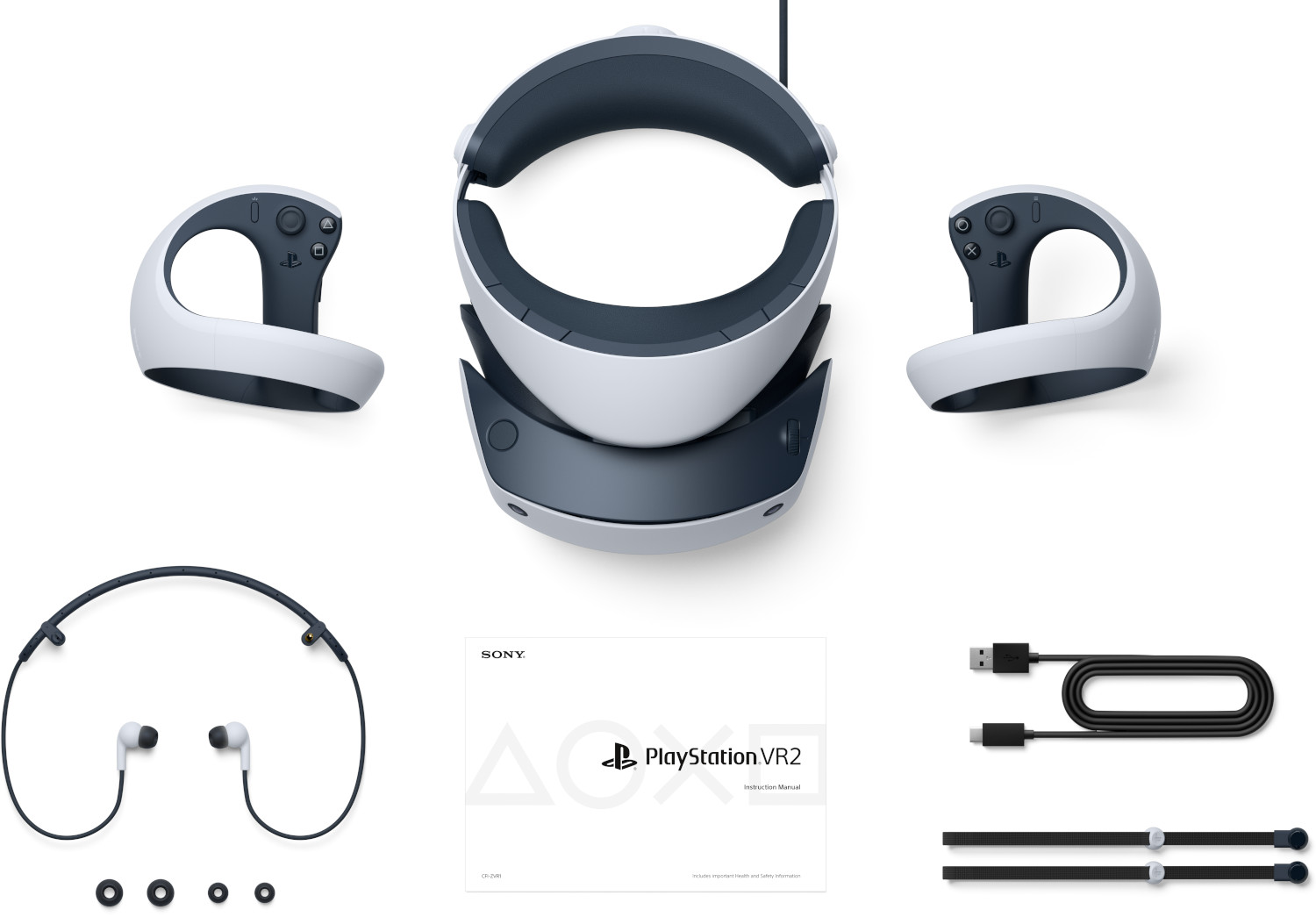 VR headset and controllers on a white surface, with wires, earbuds, and a manual.