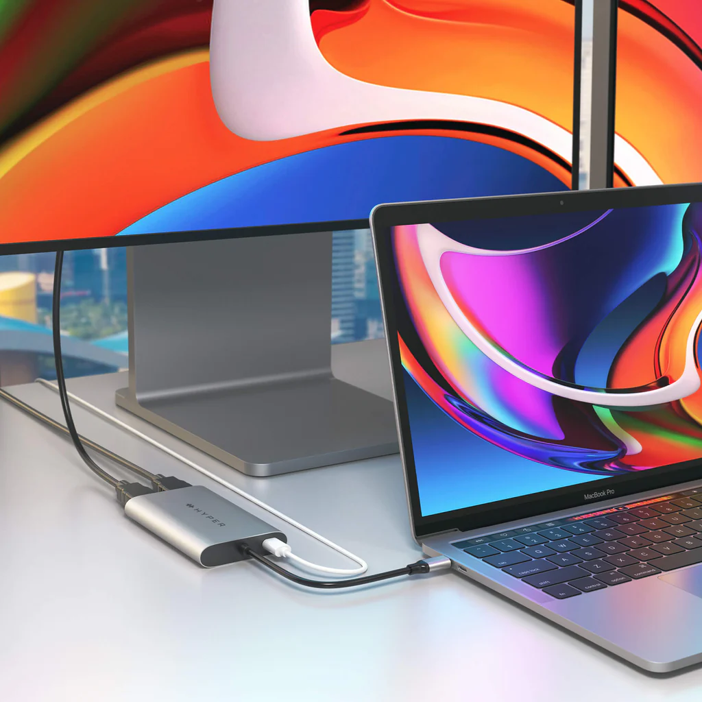 Una computadora portátil conectada a un monitor y un concentrador. La configuración está en una superficie blanca.