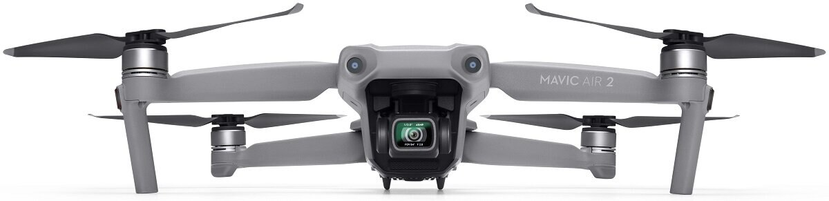 Szary dron z czterema śmigłami, kamerą i pilotem na białej powierzchni.