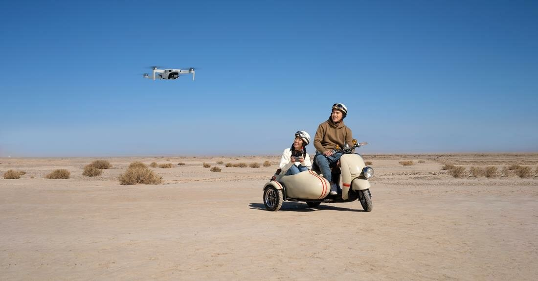 Dron lecący nad skuterem z dwiema osobami, krajobraz pustynny.