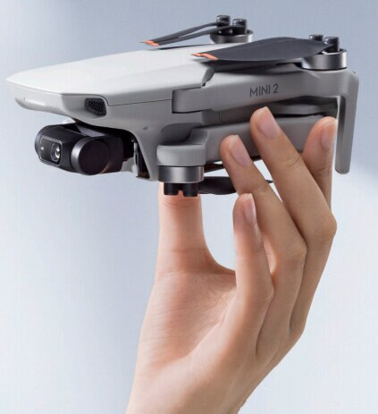 Szary dron trzymany przez rękę. Dron ma dwie śmigła, kamerę i jest w locie.