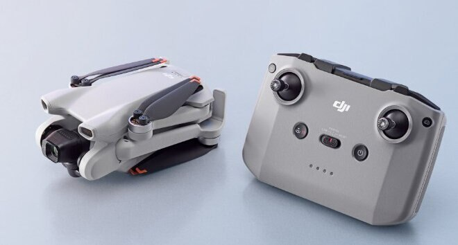 Złożony dron i jego pilot. Oba są szare i na jasnoniebieskim tle.