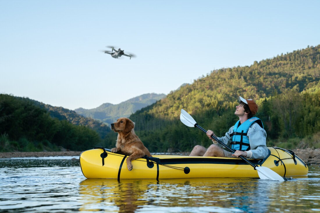 Mężczyzna i pies w żółtej kajaku, z dronem lecącym nad nimi.