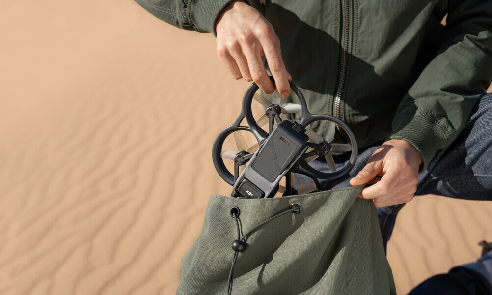 Osoba trzymająca drona i wkładająca go do zielonej torby na tle pustyni.