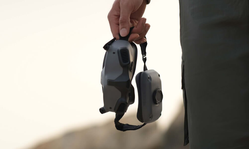 Osoba trzymająca gogle VR i kontroler, na zewnątrz, w ciągu dnia.