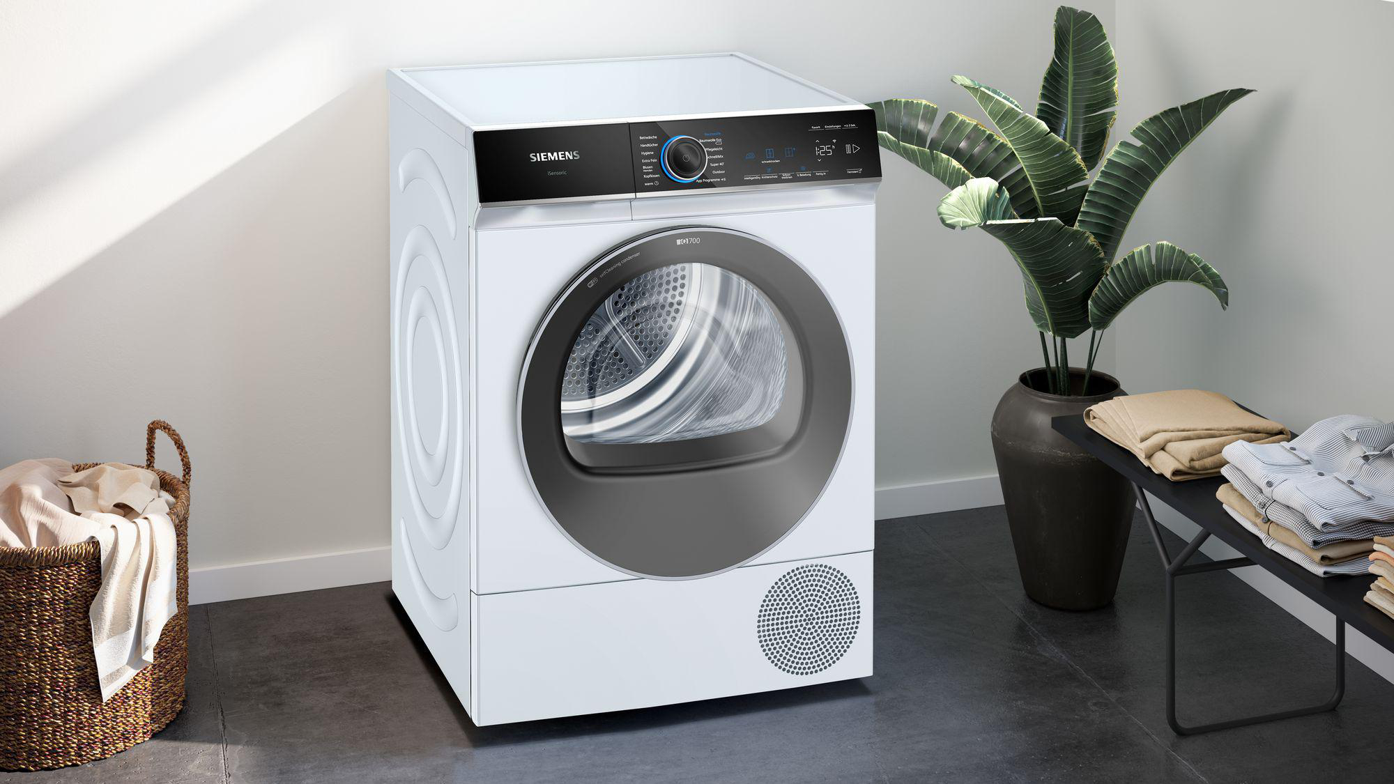 Weiße Trocknermaschine mit Wäschekorb und Pflanze. Helles, sauberes Interieur.