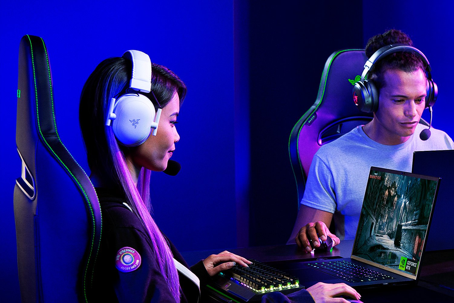 Zwei Gamer mit Headsets an Laptops. Eine Frau hat ein weißes Headset, der Mann ein grünes.