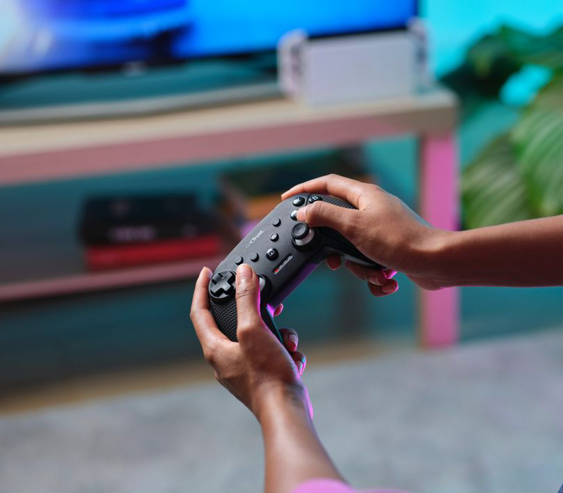 Egy személy egy szürke gamepadet tart fekete gombokkal, fekete-fehér háttérrel.