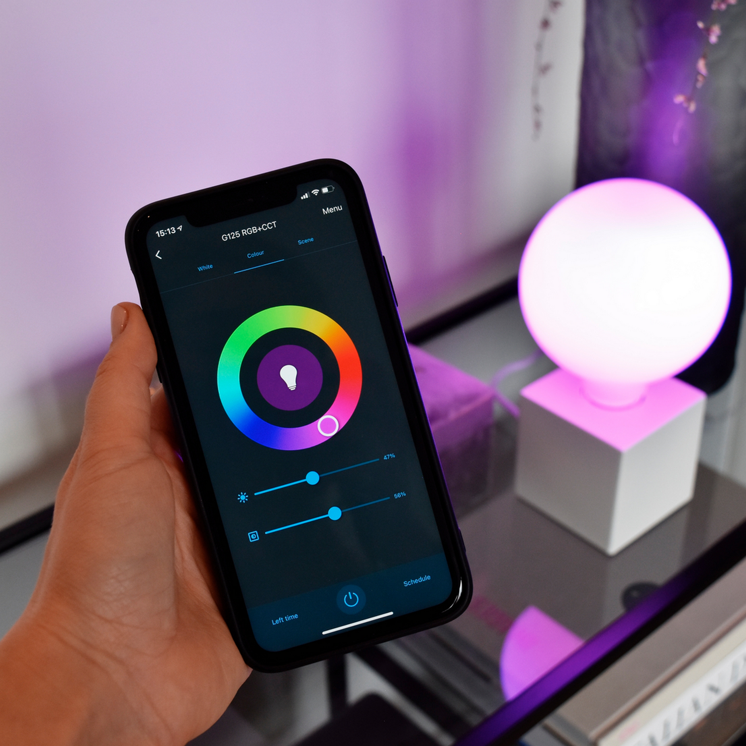 A hand holding a phone showing a smart light app, next to a glowing orb.