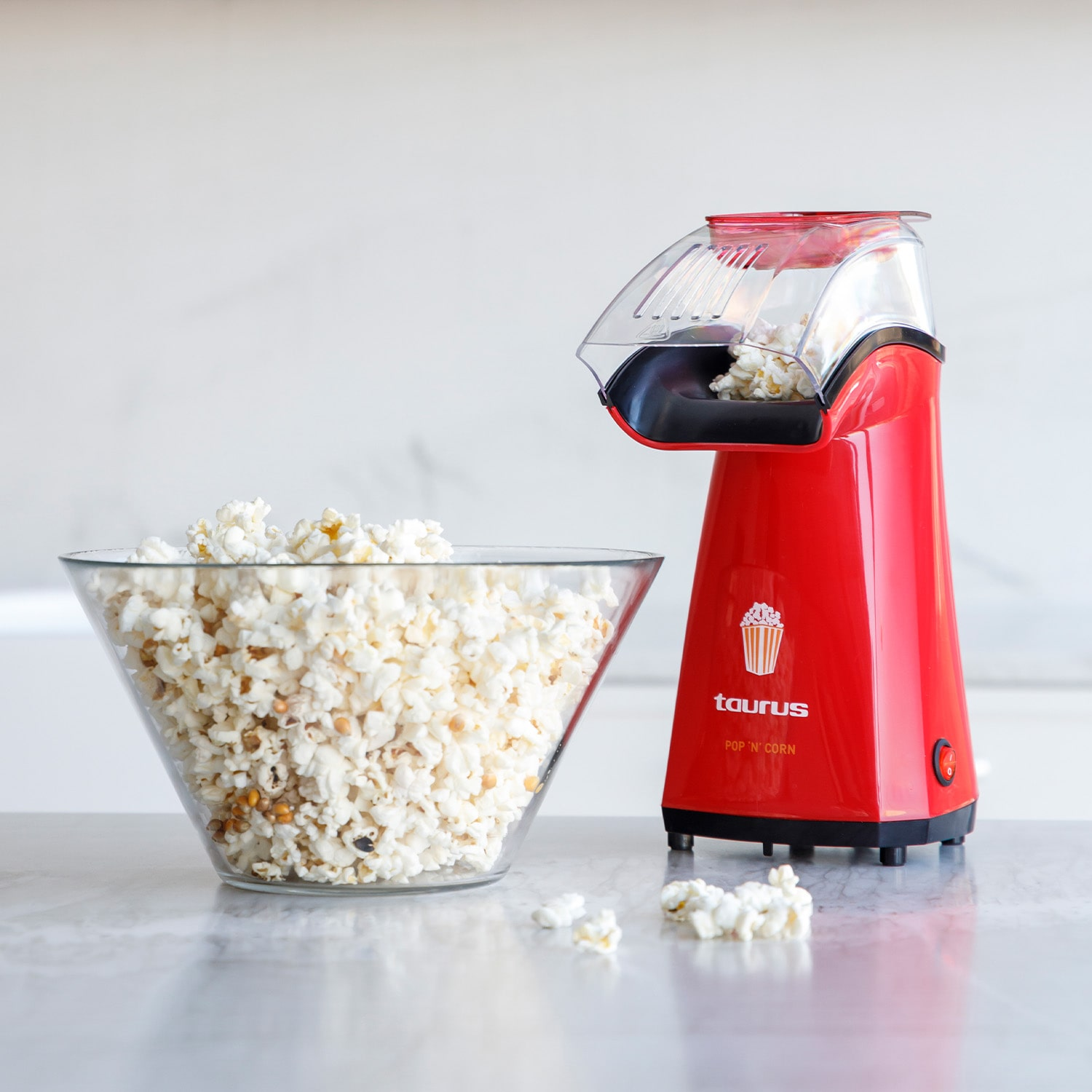 Máquina de palomitas roja con palomitas en un tazón transparente, y palomitas dispersas.