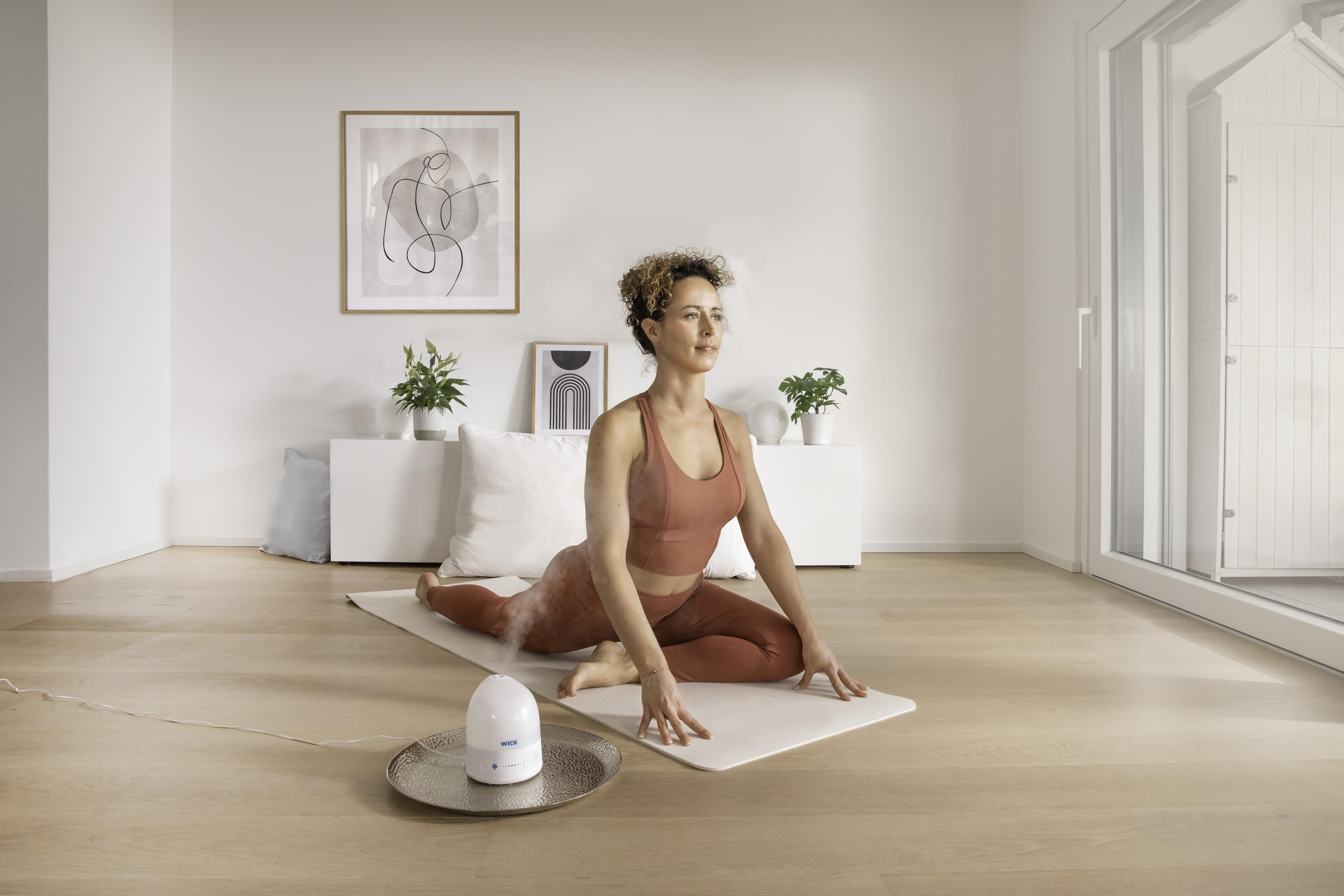 Frau macht Yoga mit einem Diffusor auf einem Tablett in hellem Raum.