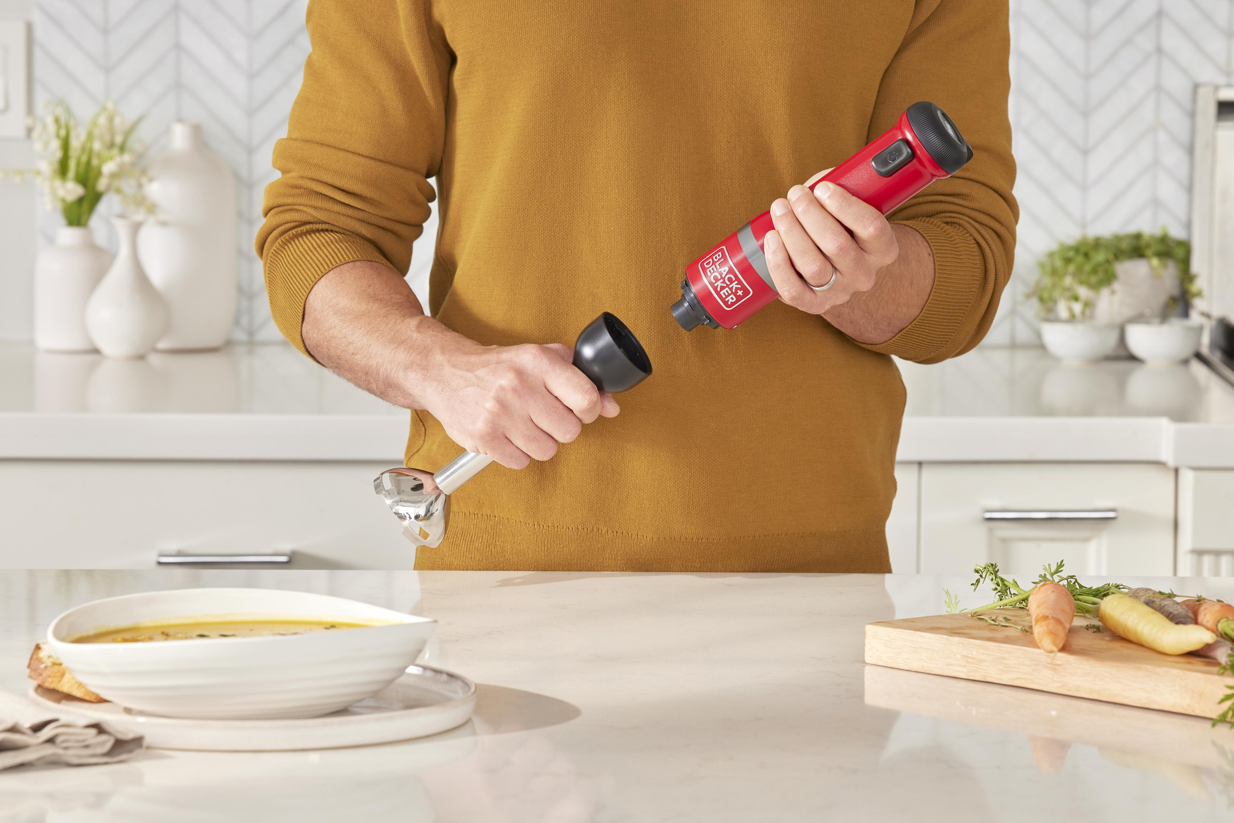 Eine Person bereitet ein Gericht zu, indem sie einen Stabmixer und eine Schüssel Suppe zusammenstellt.
