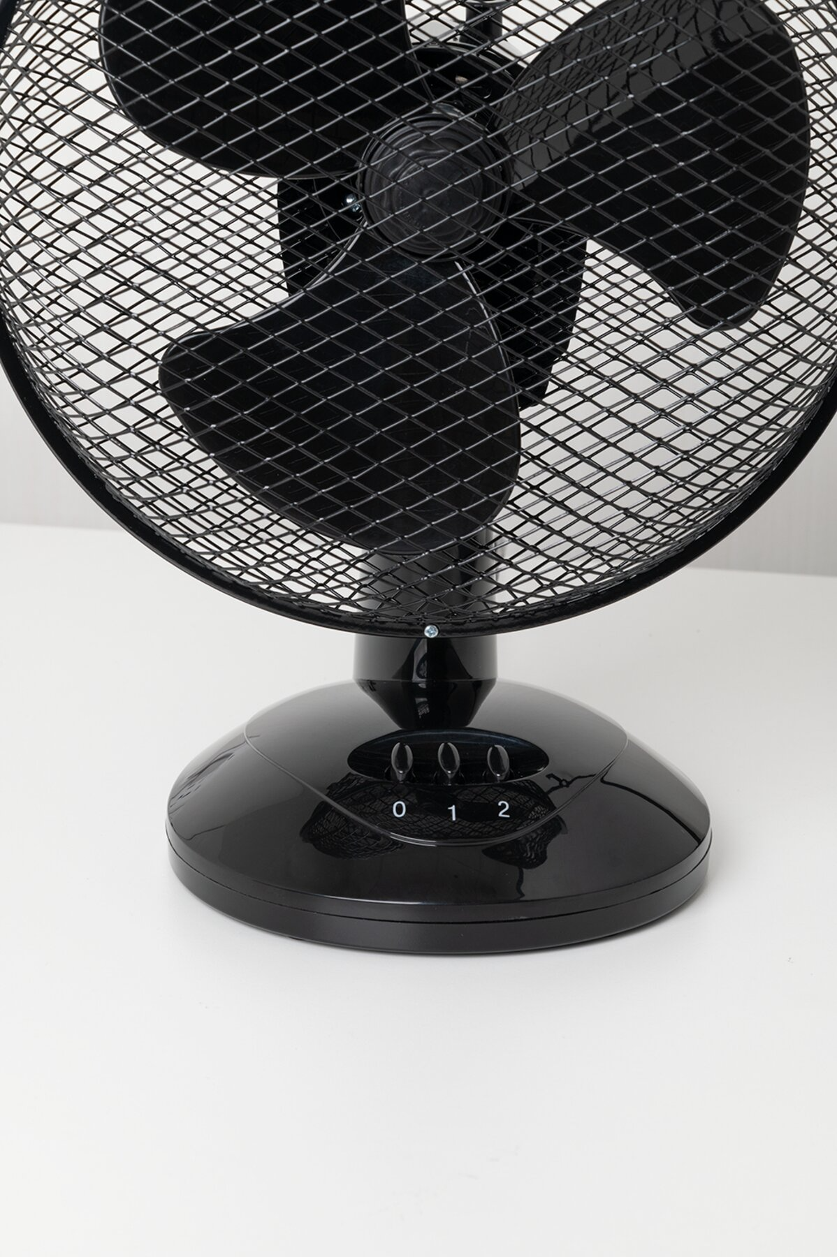 Fekete asztali ventilátor sebességbeállításokkal: 0, 1, 2. Van rajta egy rácsos védő.
