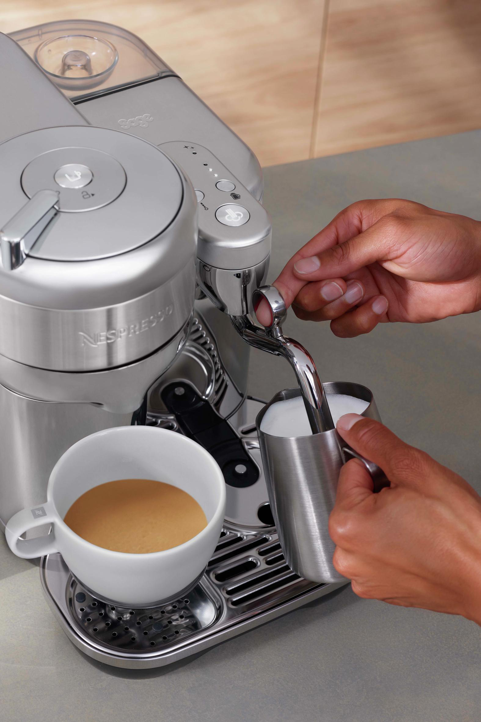 Kaffeemaschine bereitet Kaffee zu. Person gießt Milch ein.